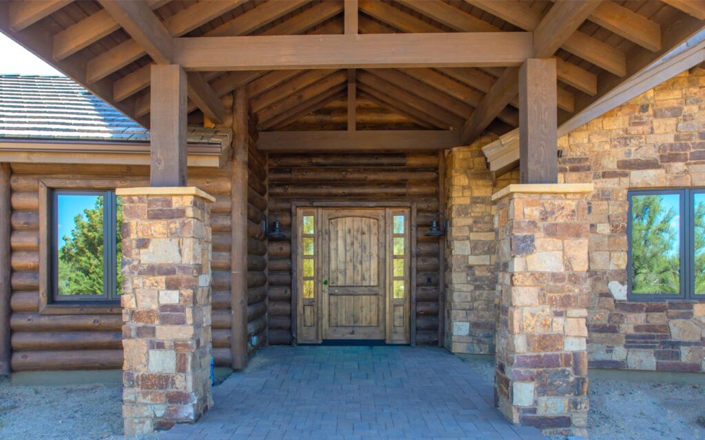 Covered front entry at Murphy’s Station with timber beams, stone columns, and wood front door in American Ranch Prescott home