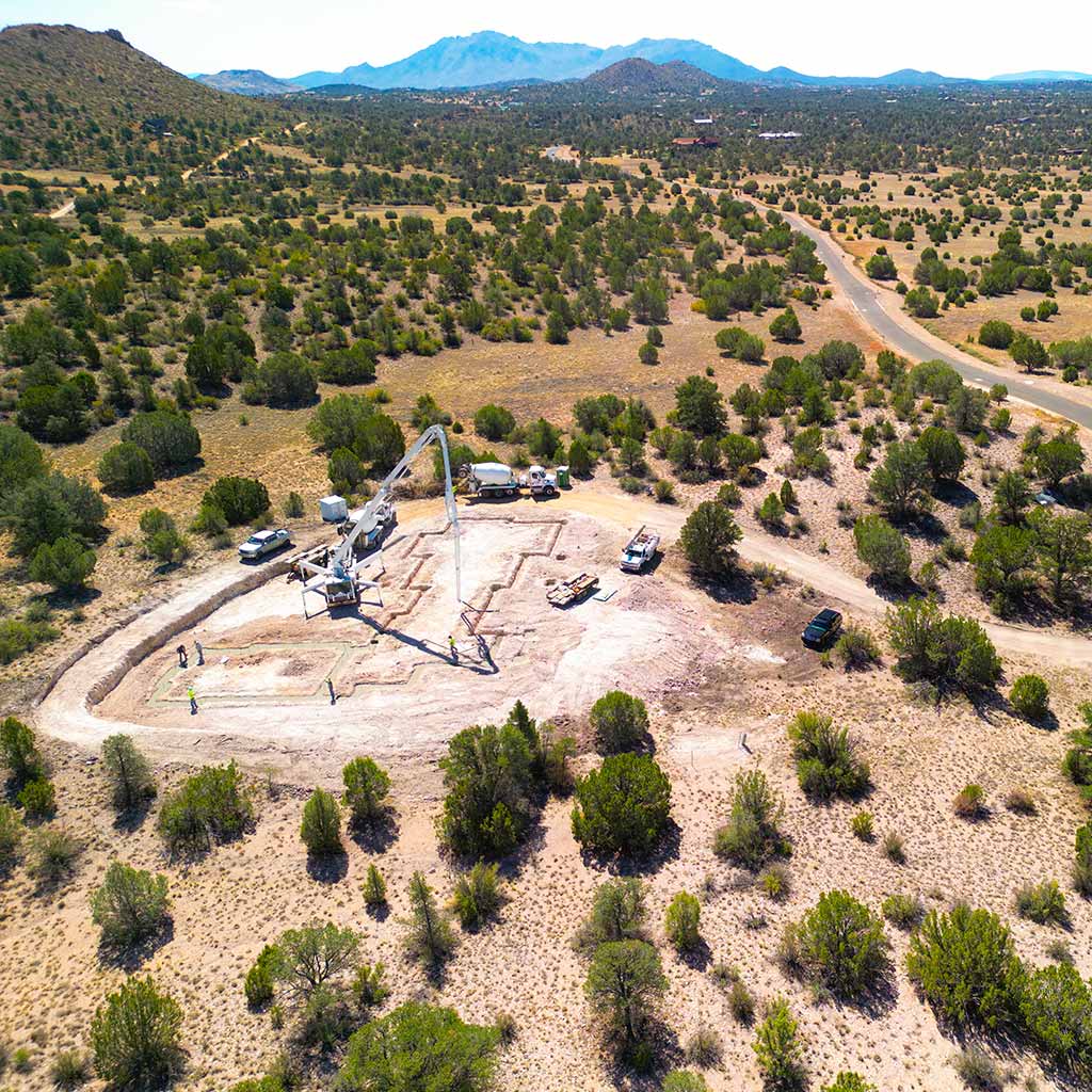 Drone view of a new custom home foundation being poured in Sterling Ranch with Williamson Valley and Granite Mountain in the background