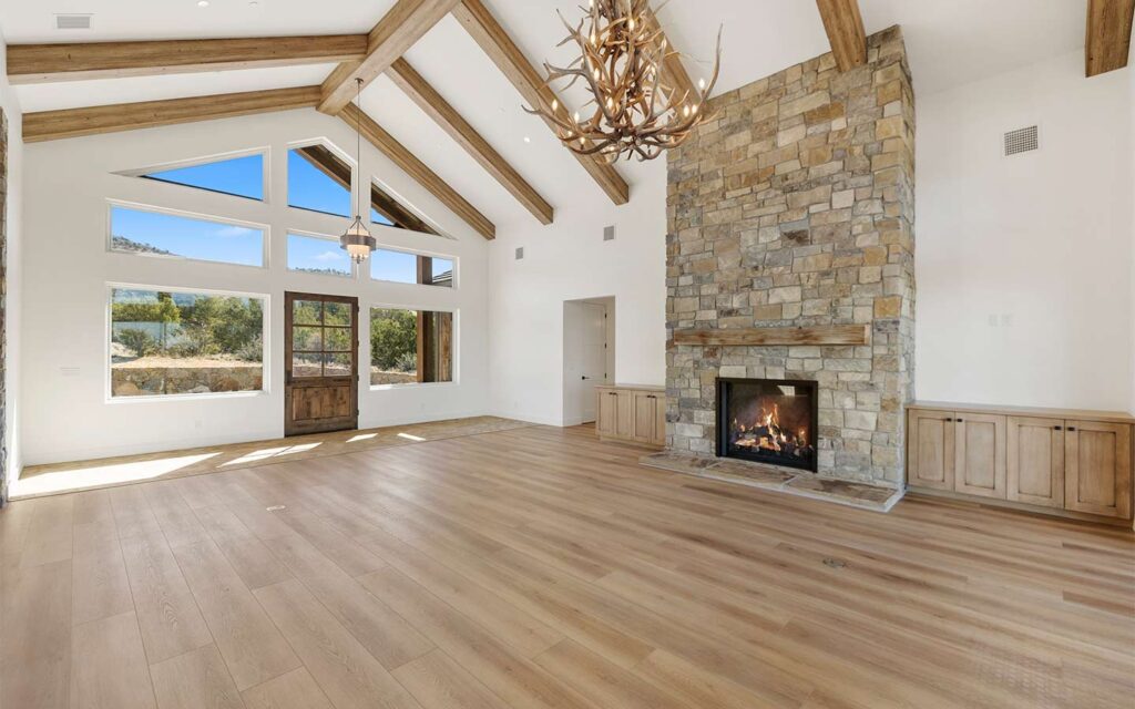 Great room with stone fireplace, vaulted ceiling, and wood beams in Sterling Ranch custom home