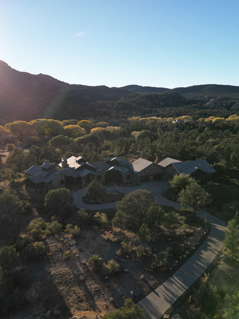 Aerial sunset view of Murphy’s Station custom home in American Ranch with pasture, trees, and high-desert skyline in the background