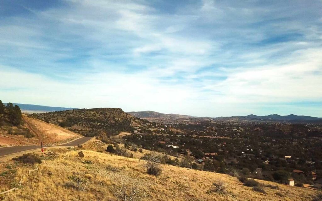Hilly desert landscape with a winding road toward a small town in the valley under a blue sky.