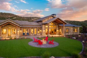 Sterling Mesa rear elevation at sunset with covered patios, reclaimed wood siding, stone detailing, fire pit, and landscaped outdoor living