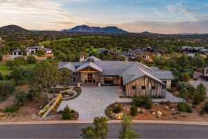 Front aerial of Silent Moon in Talking Rock Ranch Phase 12 with paver motor court, native landscaping, wood and stone exterior, and expansive Prescott mountain views