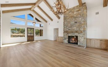 Great room with stone fireplace, vaulted ceiling, and wood beams in Sterling Ranch custom home