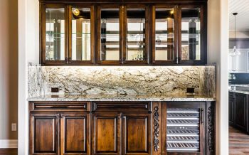 Closeup of built-in bar with glass-front cabinets, granite backsplash, and beverage fridge in Talking Rock Ranch custom home Prescott AZ