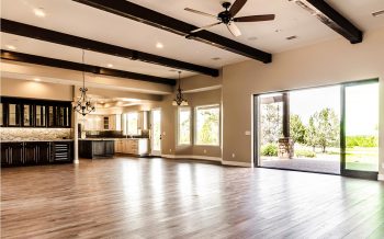 Open concept great room with beamed ceiling, hardwood floors, bar and kitchen, and sliding glass doors to patio at Kokopelli, a Talking Rock Ranch custom home